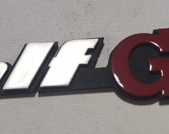 May include: A silver and black "Golf GTI" emblem with red lettering.