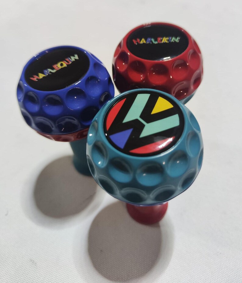 Pu&ograve; includere: Tre pomelli a forma di palla da golf con colori e design diversi. Il primo pomello &egrave; blu con la parola "HARLEQUIN" in lettere arcobaleno. Il secondo pomello &egrave; rosso con la parola "HARLEQUIN" in lettere bianche. Il terzo pomello &egrave; blu-verde con un design geometrico colorato.