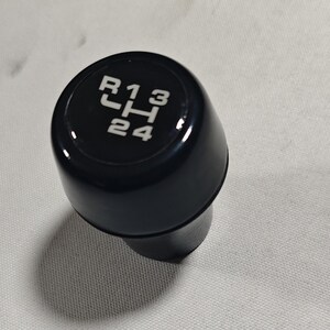 May include: Black gear shift knob with white lettering indicating the gear positions: R, 1, 3, H, 2, 4.