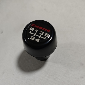 May include: Black gear shift knob with a red "Emblem" logo and white numbers and letters indicating gear positions: R, 1, 2, 3, 4, 5.