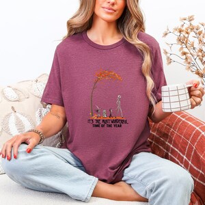 May include: Burgundy t-shirt with a graphic featuring a tree with orange leaves and characters from The Nightmare Before Christmas. The text "IT'S THE MOST WONDERFUL TIME OF THE YEAR" is below the graphic.