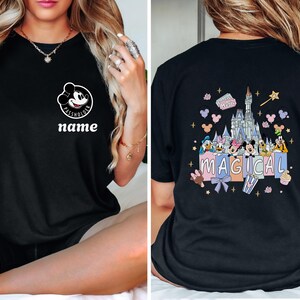 May include: Black t-shirt featuring a Mickey Mouse graphic with the text "PASS HOLDER" and "name" on the front. The back of the shirt displays a colorful illustration of Disney characters and a castle with the word "MAGICAL".