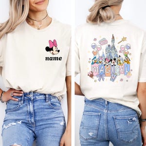 May include: Cream-colored t-shirt featuring Minnie Mouse with a pink bow and the word "name" in black. The back of the shirt displays a colorful graphic with Disney characters, a castle, and the word "MAGICAL".