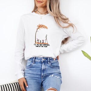 May include: White long-sleeve shirt with a graphic featuring a tree with orange leaves, and characters from The Nightmare Before Christmas. The text "IT'S THE MOST WONDERFUL TIME OF THE YEAR" is printed below the graphic.