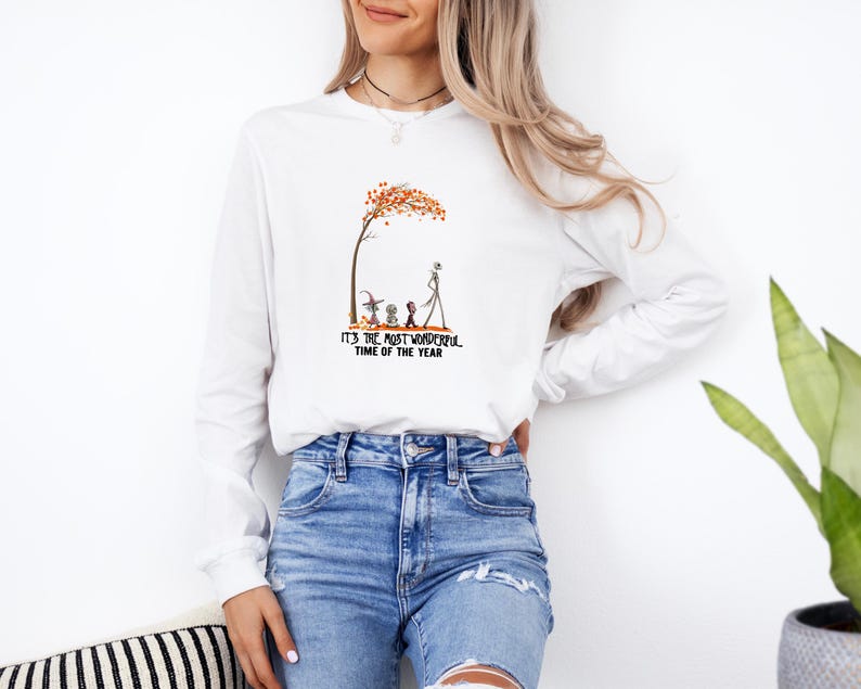 May include: White long-sleeve shirt with a graphic featuring a tree with orange leaves, and characters from The Nightmare Before Christmas. The text "IT'S THE MOST WONDERFUL TIME OF THE YEAR" is printed below the graphic.