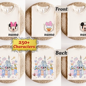 May include: Cream-colored t-shirts with cartoon character designs. The front of the shirts feature Minnie Mouse, Daisy Duck, and Mickey Mouse. The back of the shirts have a castle and the word "MAGICAL".