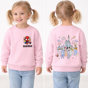 May include: Pink sweatshirt featuring a Spider-Man graphic with the word "name" below it. The back of the sweatshirt has a castle and cartoon characters with the word "MAGICAL". The child is wearing blue jeans.