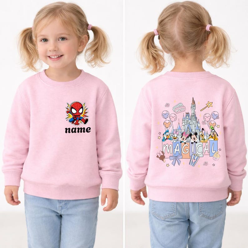 May include: Pink sweatshirt featuring a Spider-Man graphic with the word "name" below it. The back of the sweatshirt has a castle and cartoon characters with the word "MAGICAL". The child is wearing blue jeans.