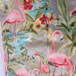 May include: A gray fabric with a tropical print featuring pink flamingos, green palm leaves, and colorful flowers. The fabric has a subtle texture and a seam down the center.