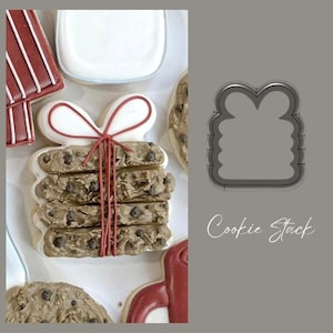 May include: A cookie cutter in the shape of a stack of cookies tied with a bow. The cutter is made of metal and has a gray finish. The text "Cookie Stack" is written below the cutter.