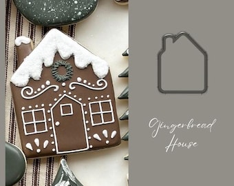 May include: A gingerbread house cookie cutter with a brown metal finish. The cutter is shaped like a gingerbread house with a roof, chimney, and windows. The text "Gingerbread House" is written below the cutter.