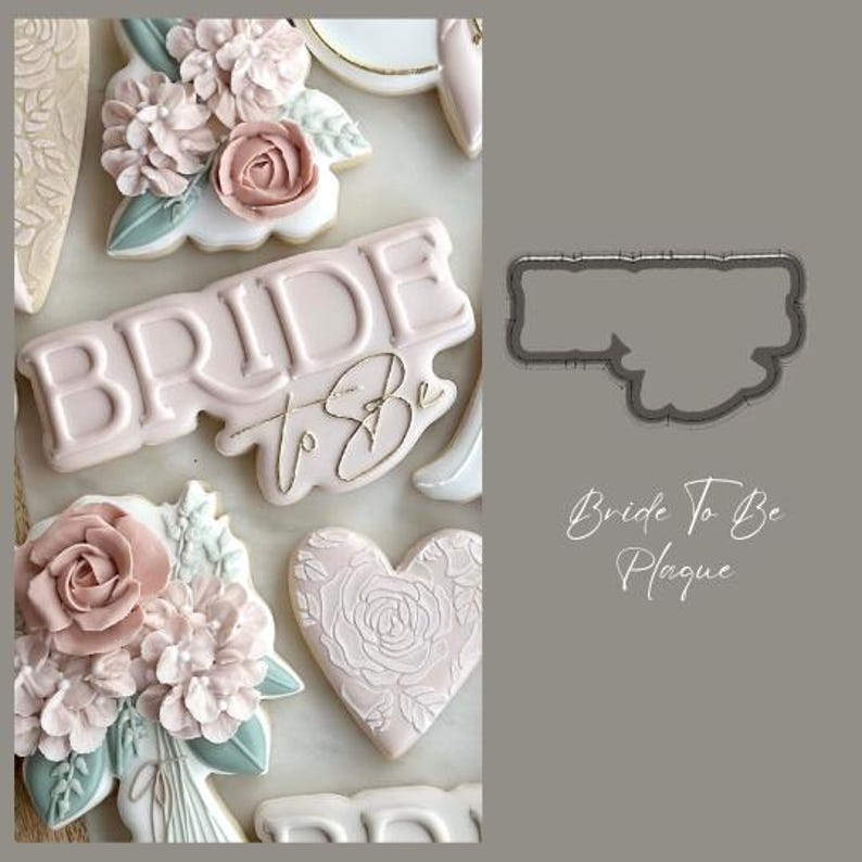 May include: A pink and white cookie decorated with the words "Bride to Be" and a floral design. The cookie is on a white surface. There is a cookie cutter in the shape of a rectangle with rounded corners.