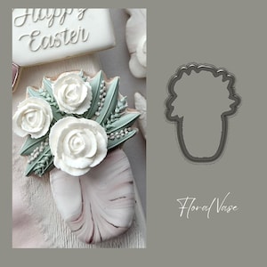 May include: A close-up of a white fondant floral arrangement in a pink and white marbled vase. The vase is decorated with a marbled effect. The flowers are white roses with green leaves. The image also shows a cookie cutter in the shape of a vase with flowers. The text "Floral Vase" is written below the cookie cutter.