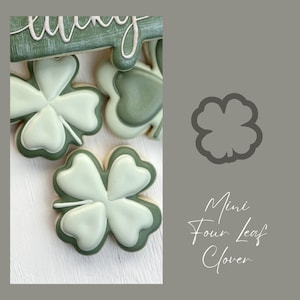 Peut inclure: Un gros plan sur un emporte-pièce en forme de trèfle à quatre feuilles. L'emporte-pièce est en métal et de couleur grise. Le texte "Mini Four Leaf Clover" est écrit sous l'emporte-pièce.