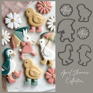 Puede incluir: Un juego de cortadores de galletas con forma de pato, conejo, ganso, gnomo y flor. Los cortadores están hechos de metal y están diseñados para crear galletas para un baby shower. El texto "April Showers Collection" está impreso en el fondo.