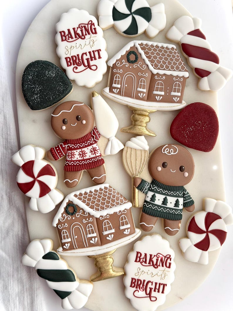 May include: A selection of festive Christmas cookies on a white surface. The cookies feature gingerbread men, gingerbread houses on golden stands, candy canes, and cookies with the text "Baking Spirits Bright" in red script.