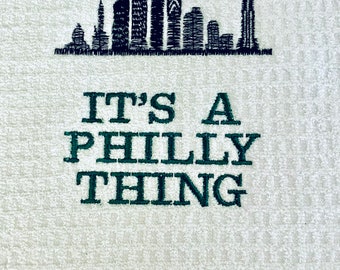 May include: A white towel with a black embroidered image of the Philadelphia skyline and the text "IT'S A PHILLY THING" in green.