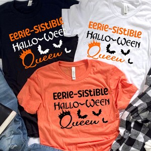 Könnte beinhalten: Drei T-Shirts mit dem Text "Eerie-Sistible Halloween Queen" und einer Krone und Fledermausgrafik. Die Shirts sind schwarz, weiß und orange.