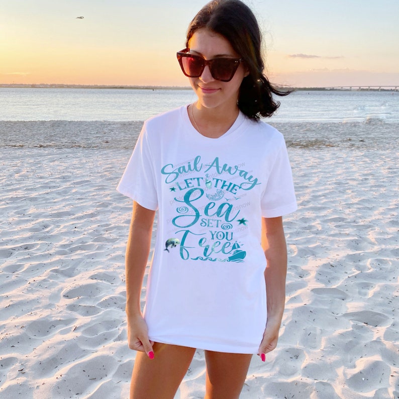 May include: White t-shirt with a teal blue graphic that says "Sail Away Let the Sea Set You Free". The graphic includes a sailboat, a dolphin, a starfish, and a seashell.