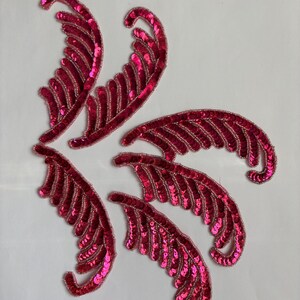 May include: Six decorative, fuchsia-colored sequin appliques in a feather design. Each applique features a curved shape with a beaded edge and rows of sequins. The appliques are arranged on a white background.