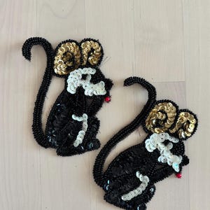 May include: Two sequined mouse appliques. The mice are black with gold sequined ears, white sequined faces, and red sequined noses. The tails are made of black beads. The appliques are on a light wood surface.