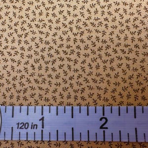 May include: Close-up of tan fabric with a repeating pattern of small, dark brown leaf-like shapes. A blue measuring tape is across the bottom, showing measurements up to 3 inches.