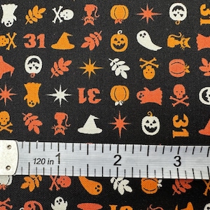 May include: Black fabric featuring a repeating Halloween pattern of orange and white pumpkins, ghosts, skulls, cats, witch hats, leaves, stars, and the number 31. A white measuring tape is placed across the bottom, showing a 4-inch scale.