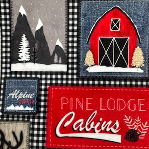 May include: A fabric with a patchwork design featuring mountain scenes, a red barn, and the text "PINE LODGE Cabins." The background is a black and white checkered pattern, creating a rustic, outdoorsy theme.