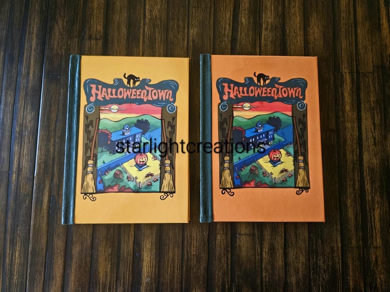 K&ouml;nnte beinhalten: Zwei B&uuml;cher mit dem Titel 'HalloweenTown' mit orangefarbenen und gelben Einb&auml;nden. Jedes Buch zeigt eine schwarze Katze, den Titel und eine farbenfrohe Illustration eines Hauses, eines K&uuml;rbisses und einer Landschaft. Die B&uuml;cher haben dunkelgr&uuml;ne Buchr&uuml;cken.