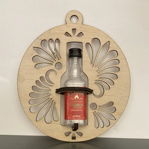 May include: A wooden ornament shaped like a circle with a decorative design. A small bottle of Jack Daniel's Tennessee Fire whiskey is displayed in the center of the ornament.