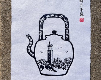 May include: A black and white print of a teapot with a clock tower inside. The teapot is decorated with leaves and flowers. The text "Campanile since 1919" is written below the teapot. The text "京都三年祭" is written in the upper right corner of the print.