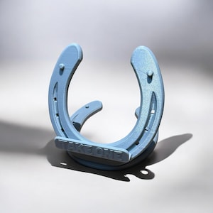 Puede incluir: Objeto en forma de herradura azul claro con el texto "TAKE ONE" en la base. La herradura tiene un diseño curvo con agujeros para clavos visibles y está hecha de un material sólido. El objeto es probablemente un artículo decorativo o un soporte.