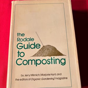 May include: A vintage book titled "The Rodale Guide to Composting" with a beige cover and green text. The cover features an illustration of a compost pile and a gardening tool. The book is by Jerry Minnich, Marjorie Hunt, and the editors of Organic Gardening magazine.
