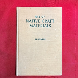 May include: A vintage book titled "USE OF NATIVE CRAFT MATERIALS" by Shanklin. The book has a light beige cover with the title and author's name in dark teal lettering. The book is set against a red background.