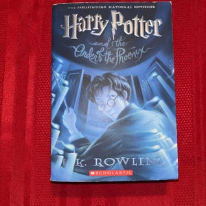 May include: A copy of "Harry Potter and the Order of the Phoenix" by J.K. Rowling. The book's cover is predominantly blue, with an illustration of Harry Potter. The title is in a stylized font. The Scholastic logo is present.