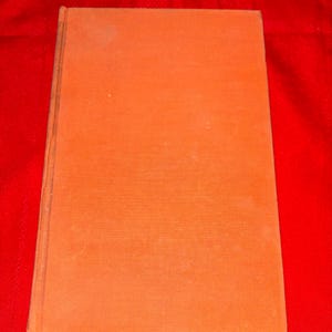 May include: An orange-colored book with a textured cover. The book is rectangular and appears to be closed. The background is a solid red color.