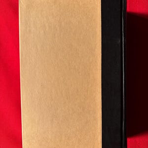 May include: A brown book with a black spine. The book is on a red surface.