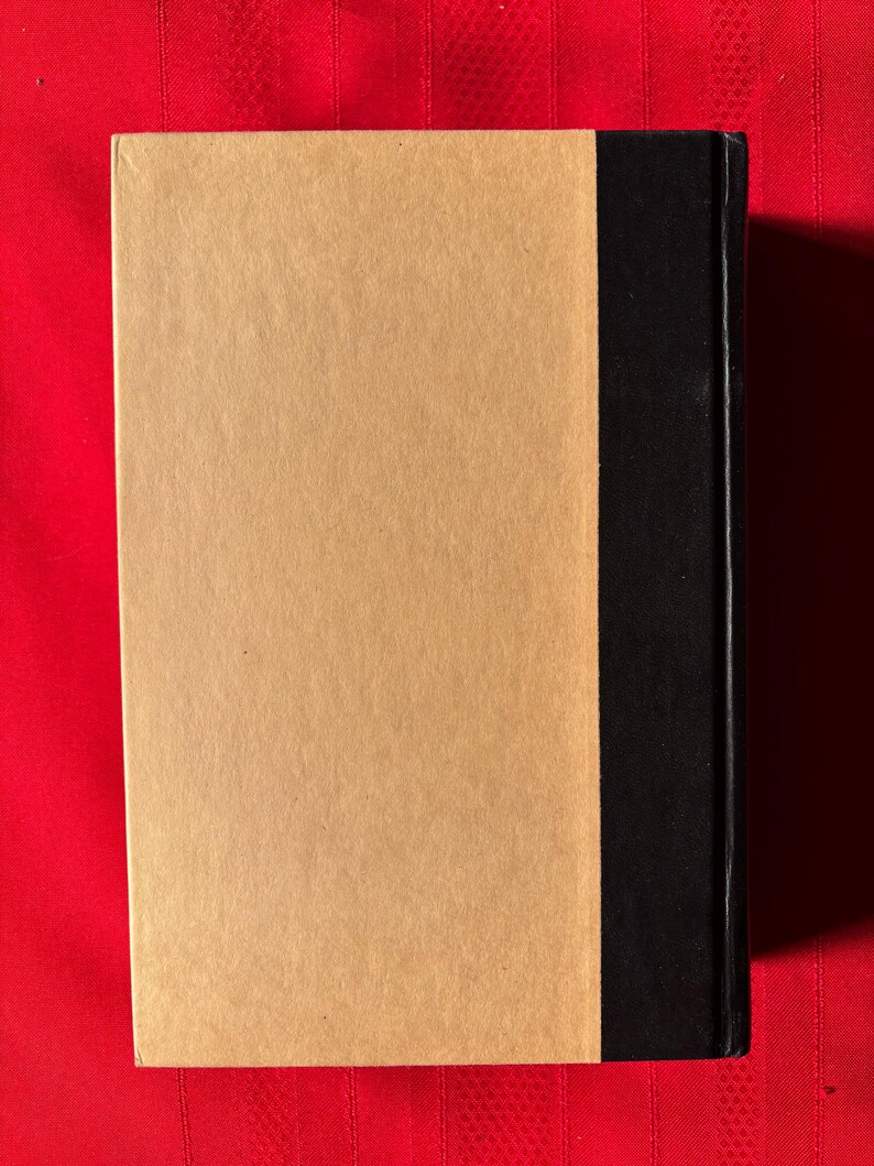 May include: A brown book with a black spine. The book is on a red surface.