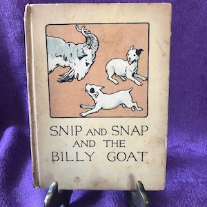 May include: A vintage book with a tan cover and a black and white illustration of a dog and a goat. The title of the book is 'SNIP AND SNAP AND THE BILLY GOAT'.