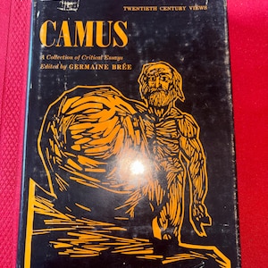 May include: A vintage book titled "Camus" with a black cover and orange graphic of a man. The book is part of the "Twentieth Century Views" series and edited by Germaine Brée. The cover has some wear and tear.