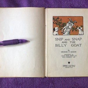 May include: An open book with a white background and a brown and orange illustration of two dogs and a goat on the right page. The title of the book is 'Snip and Snap and the Billy Goat' by George C. Mason. The book is published by P.F. Volland & Co. Chicago, U.S.A.