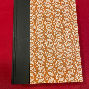 Może przedstawiać: Twarda oprawa książki z czarnym grzbietem i brązową okładką z białym wzorem kwiatowym.