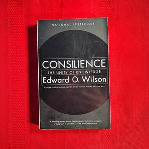 May include: A black and white book cover with the title "Consilience: The Unity of Knowledge" by Edward O. Wilson. The book cover also includes the text "National Bestseller" and "Pulitzer Prize-winning author of On Human Nature and The Ants".