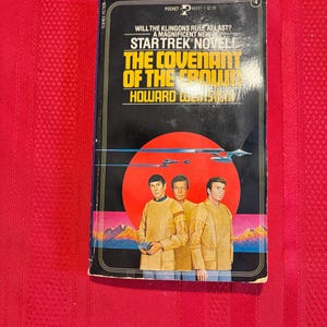 Puede incluir: Un libro de bolsillo vintage titulado "Star Trek Novel: The Covenant of the Crown" de Howard Weinstein. La portada presenta tres figuras con uniformes dorados sobre un fondo rojo con una nave espacial y una cordillera.