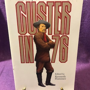 Könnte beinhalten: Buchcover von "Custer in '76" von Walter Camp, herausgegeben von Kenneth Hammer. Es zeigt ein Porträt eines Mannes in brauner Kleidung und Hut, mit dem Titel in großen, fetten Buchstaben. Der Hintergrund ist einfarbig weiß.