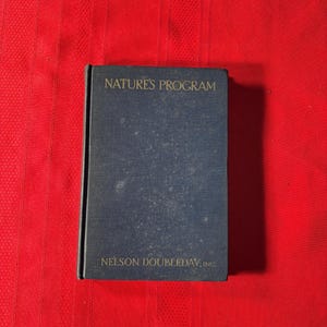 May include: A dark blue book with the title "NATURE'S PROGRAM" and the publisher "NELSON DOUBLEDAY, INC." in gold lettering. The book is on a red background.