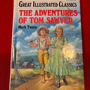 Op de afbeelding: Een vintage exemplaar van "De avonturen van Tom Sawyer" van Mark Twain. De boekomslag toont een illustratie van twee kinderen die op een zandpad lopen. De titel staat in grote rode letters, met de serietitel "Great Illustrated Classics" erboven.