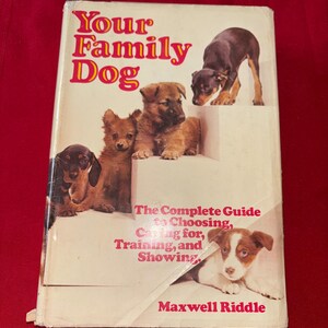 May include: A well-worn book, "Your Family Dog", featuring several puppy illustrations. The cover text includes "The Complete Guide to Choosing, Caring for, Training, and Showing." The author's name, Maxwell Riddle, is printed at the bottom.