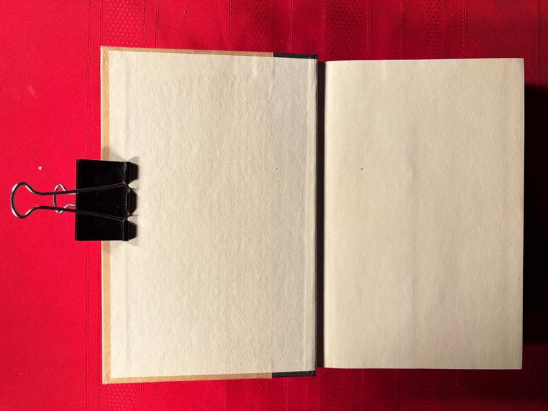 May include: An open book with blank pages, the pages are cream colored and the cover is brown. The book is lying open on a red surface.