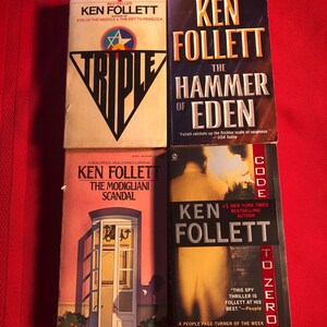May include: Four paperback books by Ken Follett, stacked vertically. The titles are "Triple", "The Hammer of Eden", "The Modigliani Scandal", and "Code to Zero".